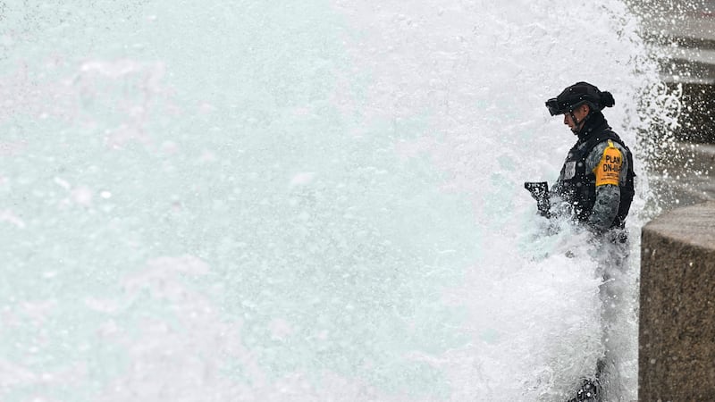 A National Guard stands in the spray as a wave hits the seawall brought by the approaching...