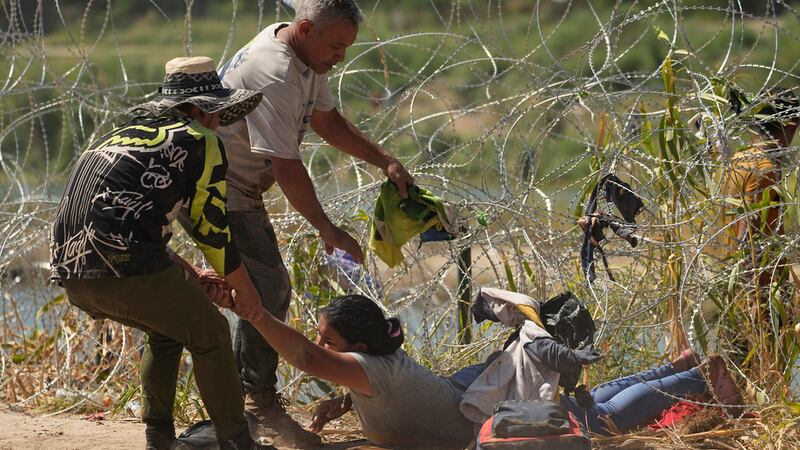 Una inmigrante que cruzó a Estados Unidos desde México es auxiliada a pasar debajo de alambre...
