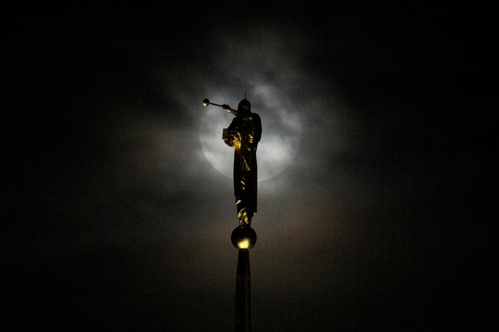 La superluna se deja ver detrás de una densa capa de nubes cerca de una estatua del ángel de...