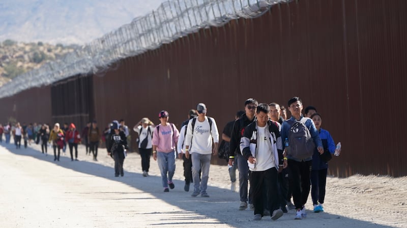 FILE - A group of people, including many from China, walk along the wall after crossing the...
