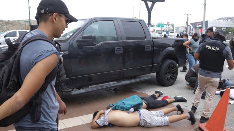 Hombres yacen boca abajo en el suelo detenidos por policías afuera de TC Televisión, luego de...