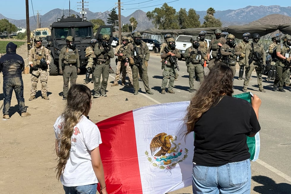 Manifestantes sostienen una bandera frente a agentes federales que bloquean un camino durante...
