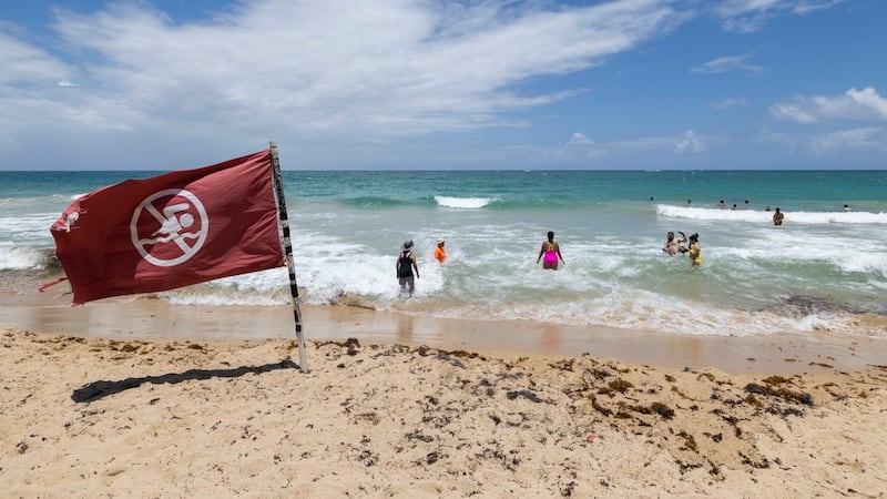 Una bandera de advertencia ondea al viento en una playa mientras la gente se baña en Condado,...