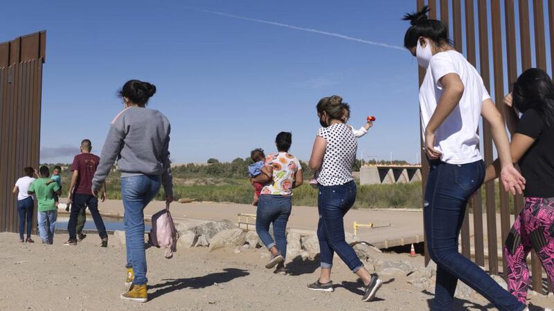 Un grupo de migrantes cruza por una apertura en la frontera entre Estados Unidos y México, en...