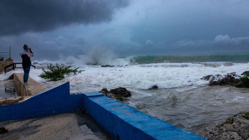 Una mujer toma fotos de las olas que chocan contra un rompeolas mientras el huracán Ian pasa...