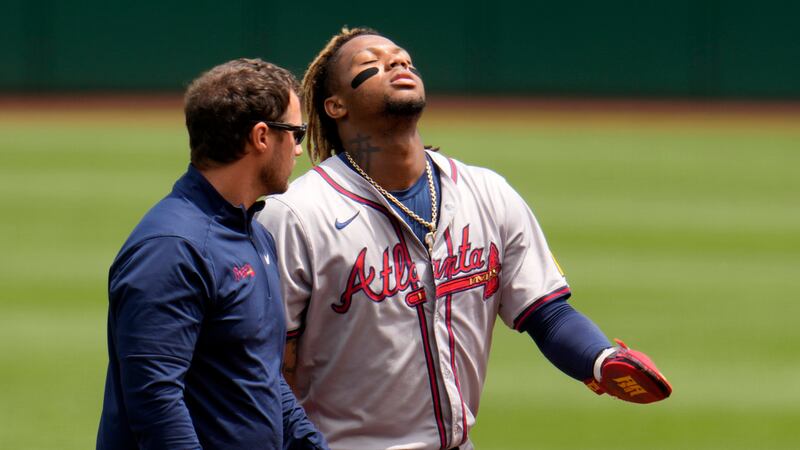 Ronald Acuña Jr., derecha, de los Bravos de Atlanta, camina para abandonar el campo acompañado...