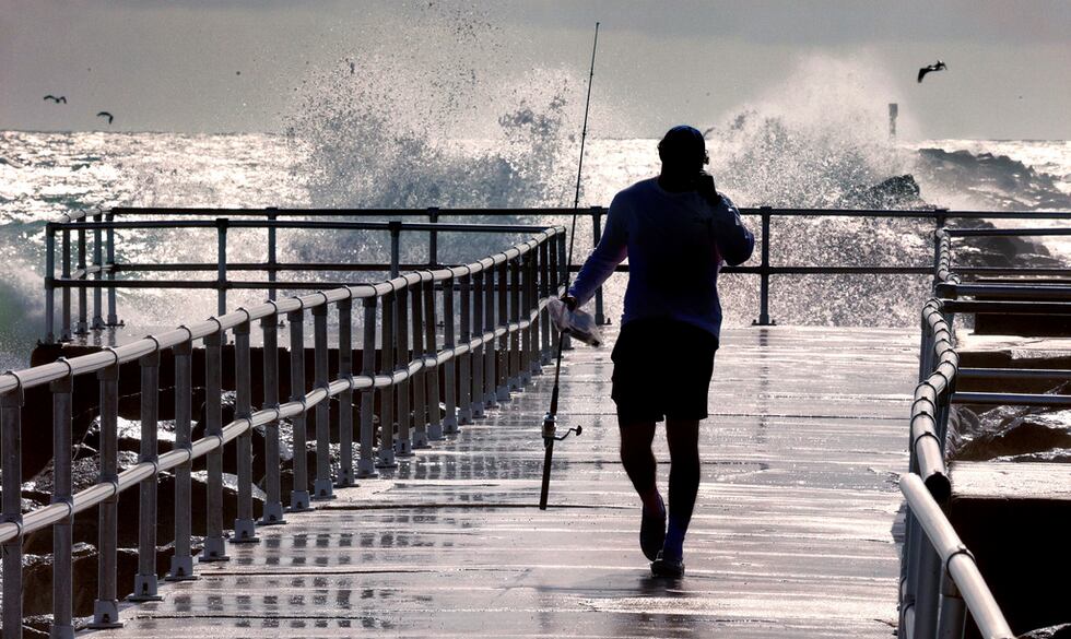 Un pescador camina por un muelle mientras granes olas generadas por el huracán Erin se...