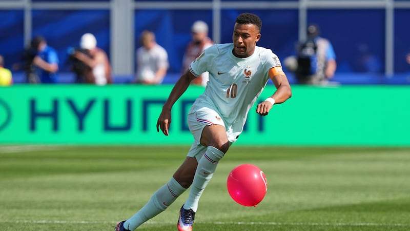 El delantero francés Kylian Mbappé (10) persigue el balón mientras un globo asoma en la cancha...