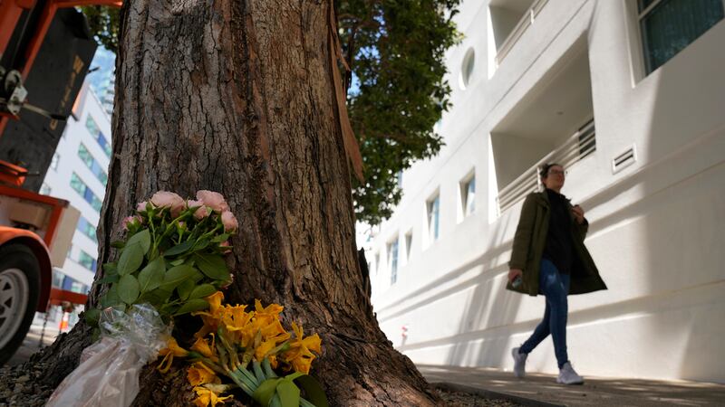 Una mujer camina el miércoles 5 de abril de 2023 frente a unas flores dejadas fuera de un...