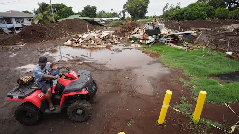 Un hombre se desplaza con su hijo cerca de una casa destruida el mes anterior al paso del...