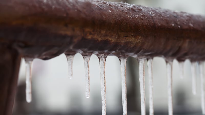 Icicles hanging from a brown pipe. Frozen water and metal surface, winter time concept....
