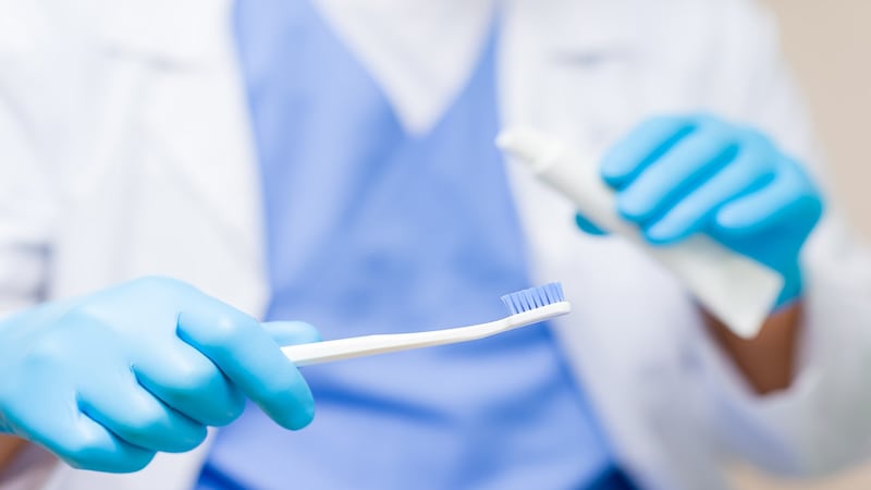 A dental hygienist holds a toothbrush and toothpaste.
